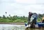 Mechanic tilting up an outboard engine on a small boat near palm trees